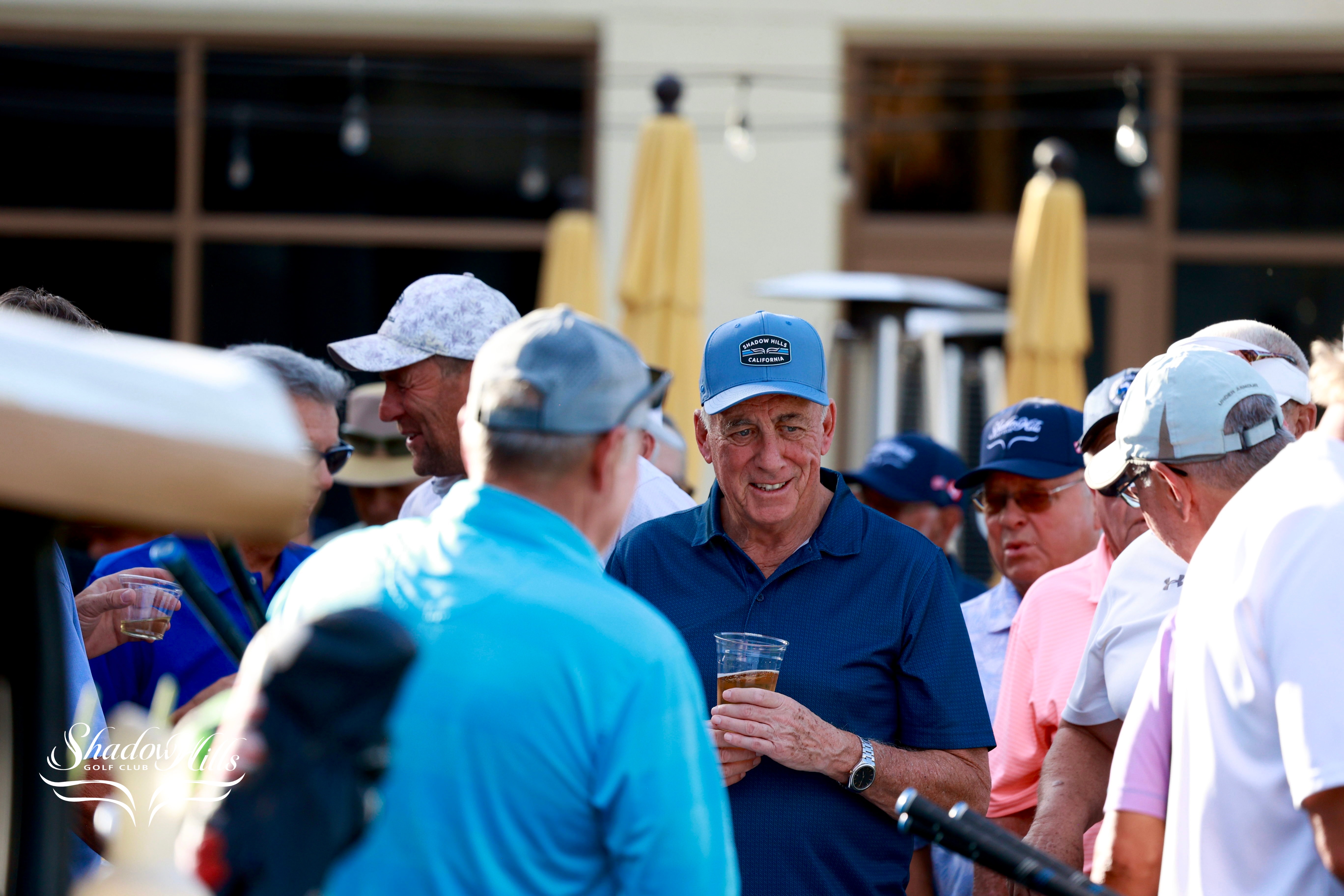 A group of golfers stands together outdoors, with one person holding a drink while conversing with others.
