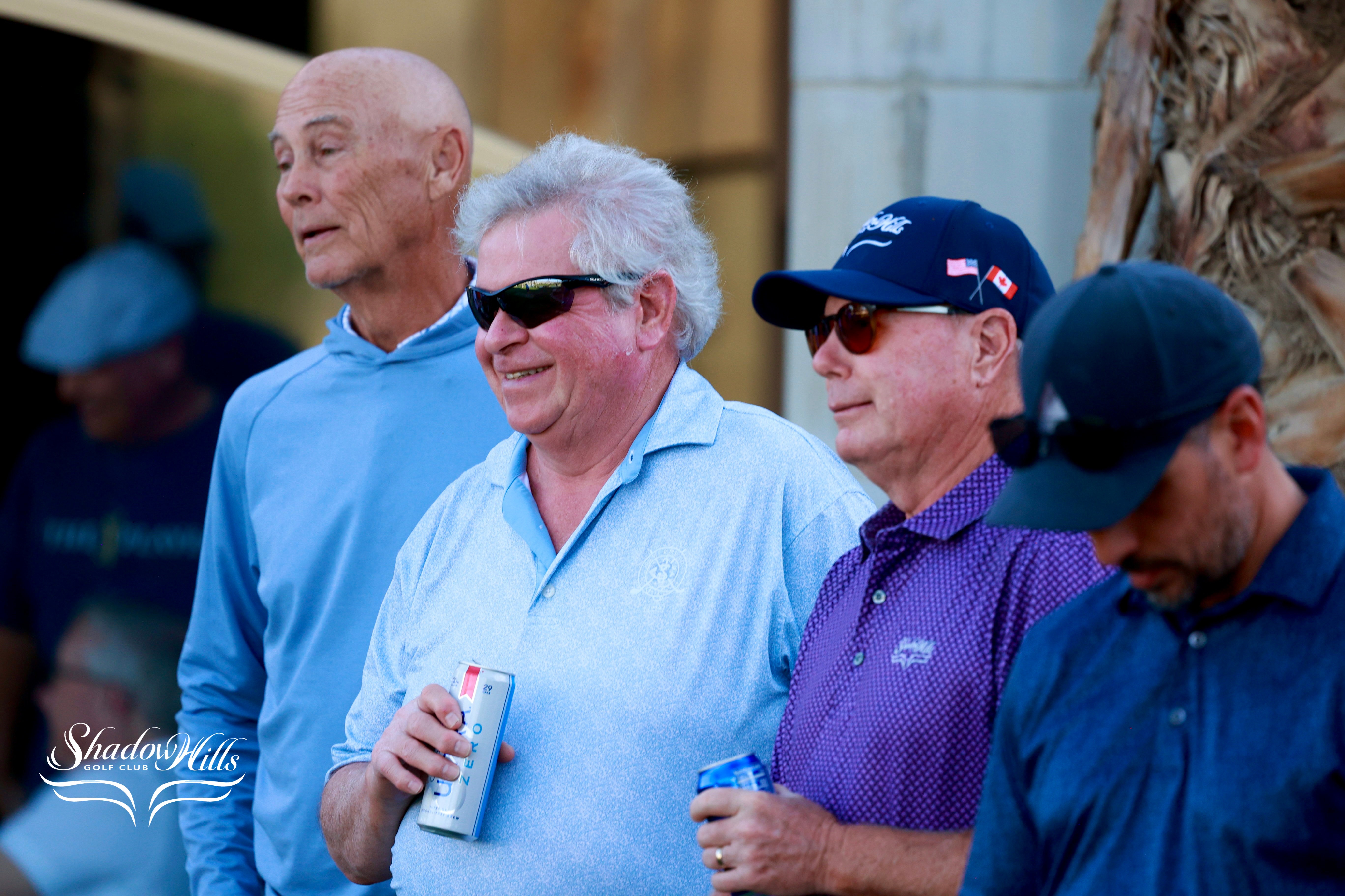 Several golfers stand together near the clubhouse, some holding drinks as they watch the event.