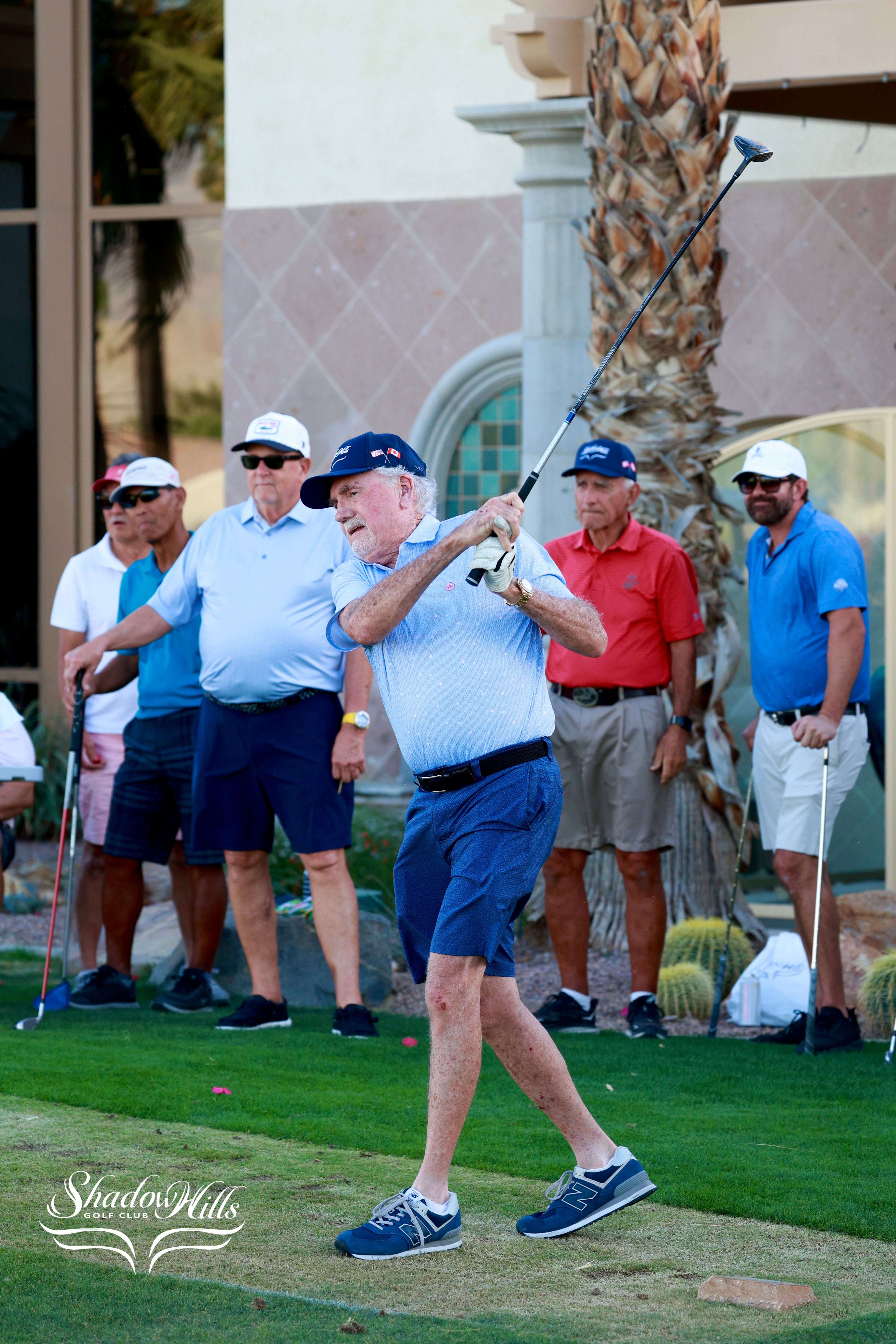 A golfer completes a follow‑through on a tee shot while other golfers wait behind him.