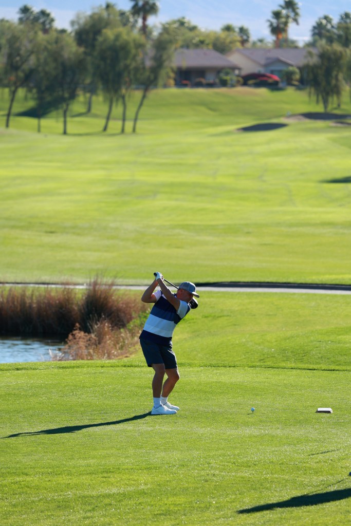 A golfer takes a full swing on a sunny fairway overlooking rolling greens.